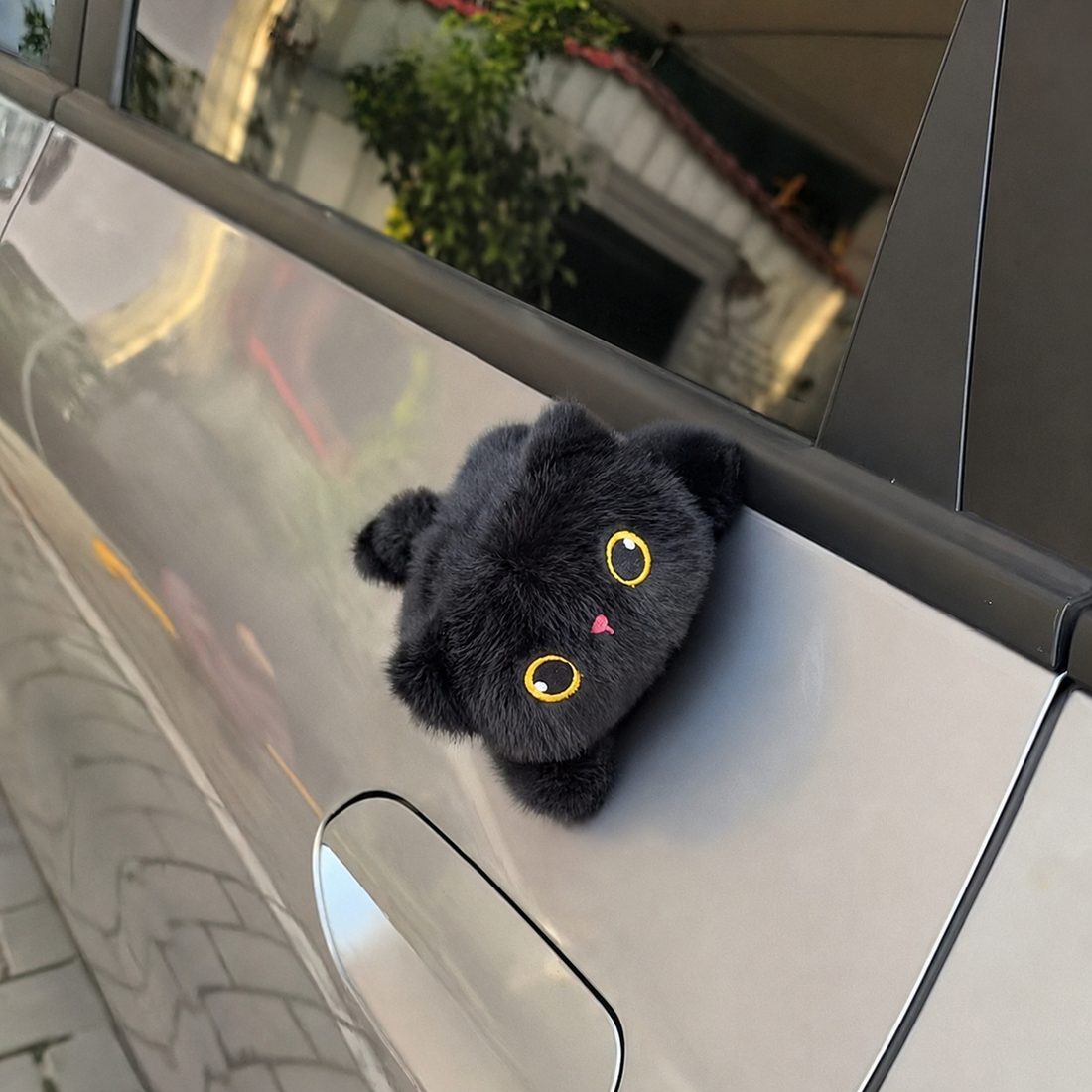 Magnetic plush cat clinging to the side of a car